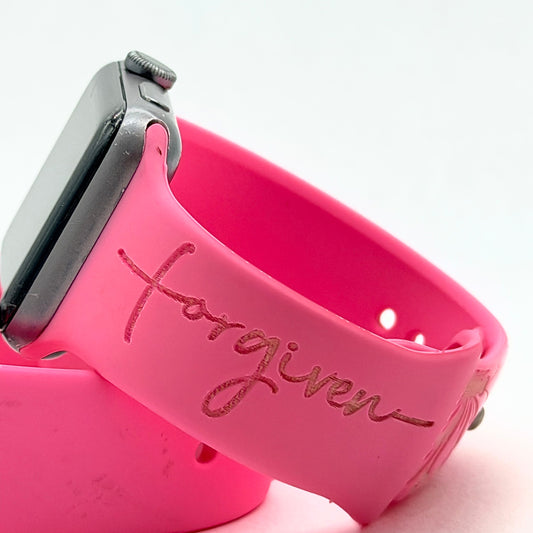 Close-up of the Forgiven script engraving on a pink silicone watch band for Apple Watch