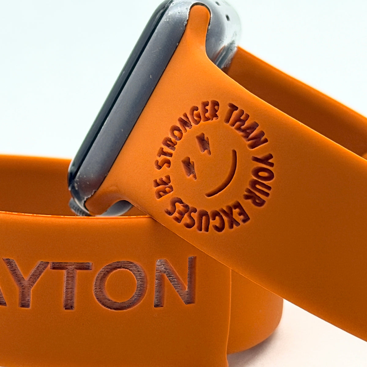 Close-up of the Be Stronger Than Your Excuses smiley engraving on a rust silicone watch band for Apple Watch