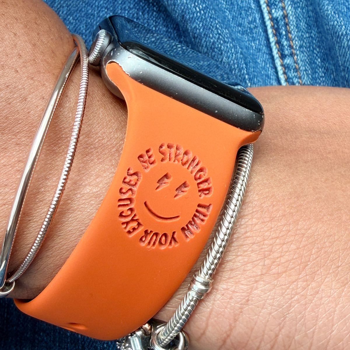 Rust Be Stronger Than Your Excuses watch band for Apple Watch worn on a wrist with silver bracelets