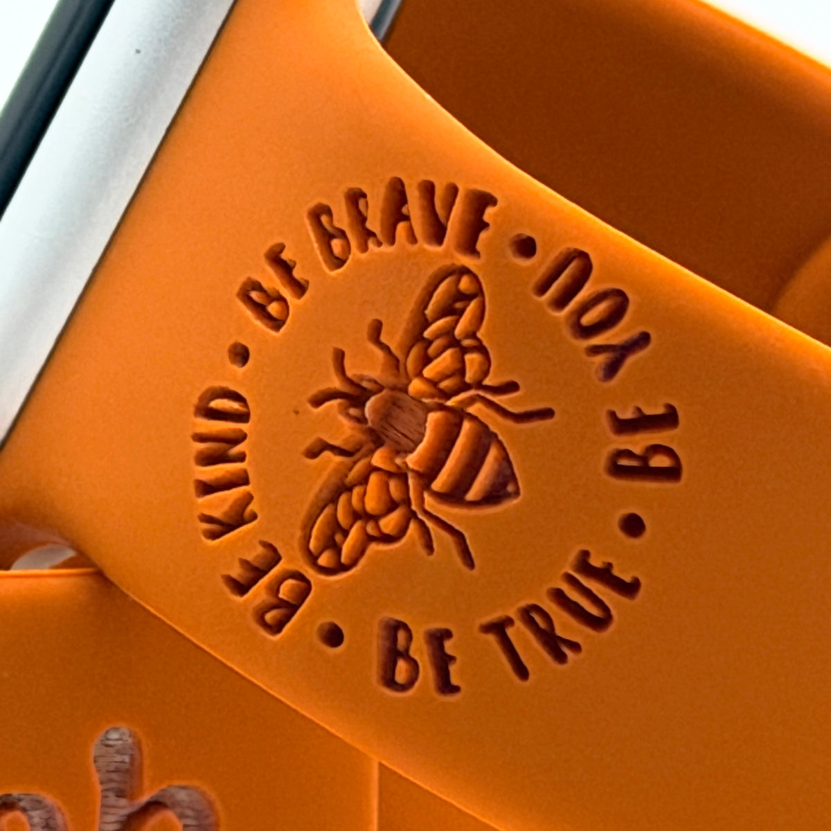 Engraving detail of the Be Kind Be Brave Bee design on a rust silicone Brave watch band for Apple Watch