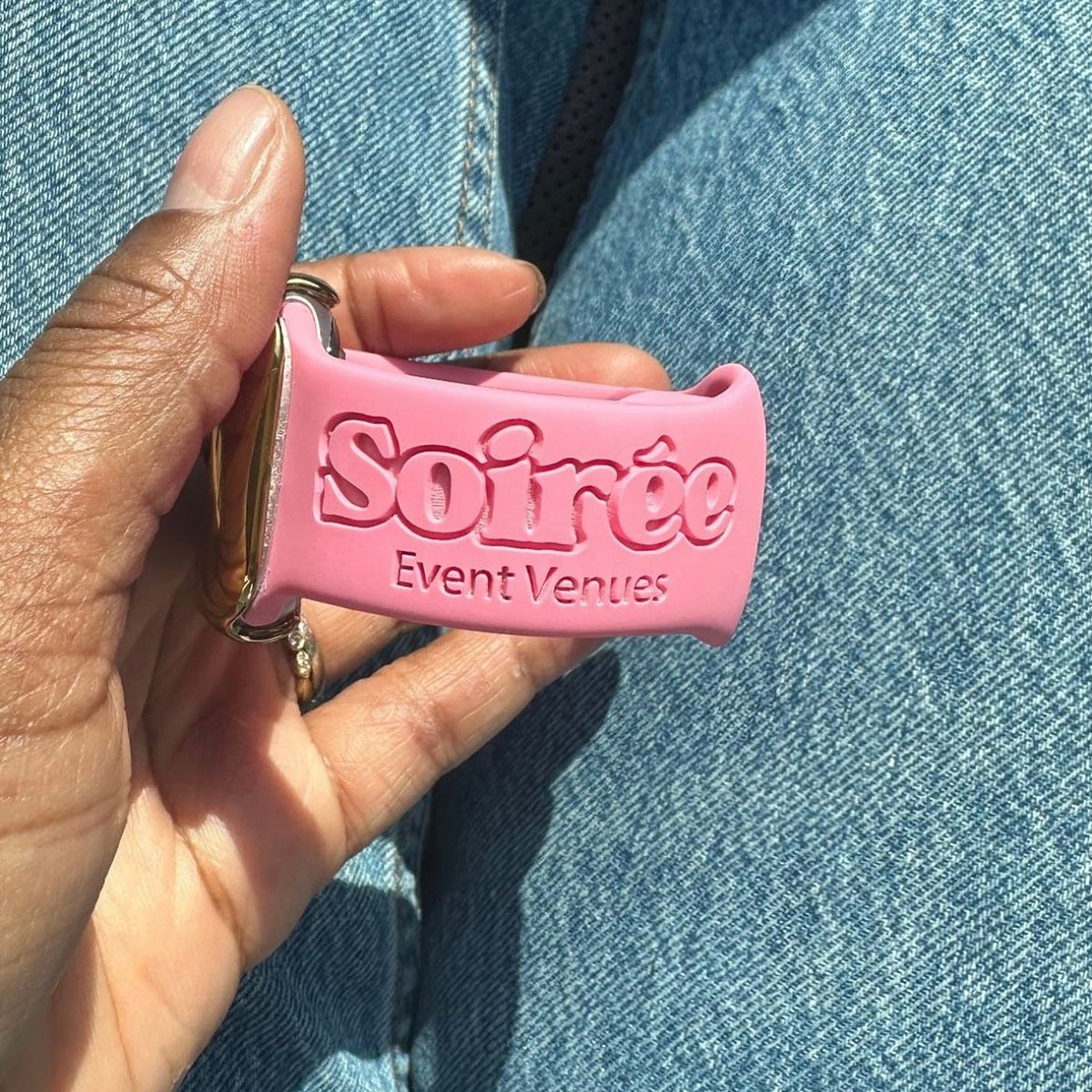 Pink silicone watch band for Apple Watch engraved with a custom business logo, held in a hand