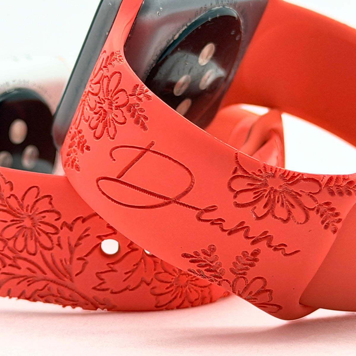 Close-up of a custom name and daisy floral engraving on a red silicone watch band for Apple Watch