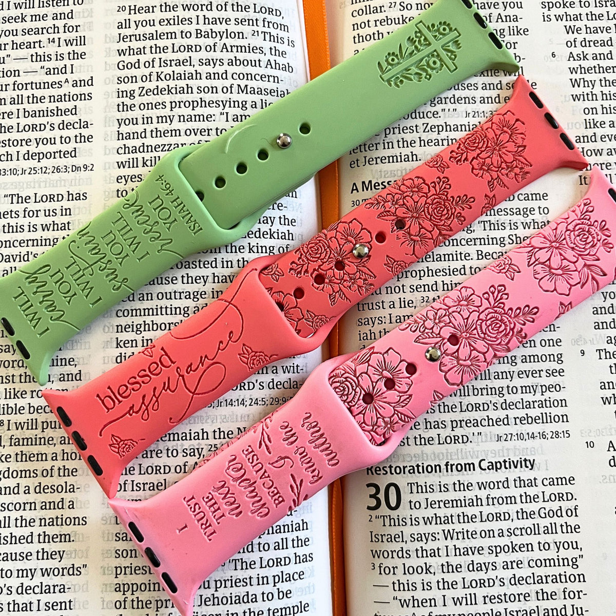 Green, coral and pink faith engraved watch band for Apple Watchs laid across an open Bible