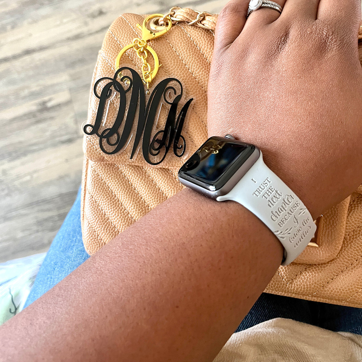 Grey I Trust the Author engraved watch band for Apple Watch worn on a wrist resting on a tan handbag with a monogram charm