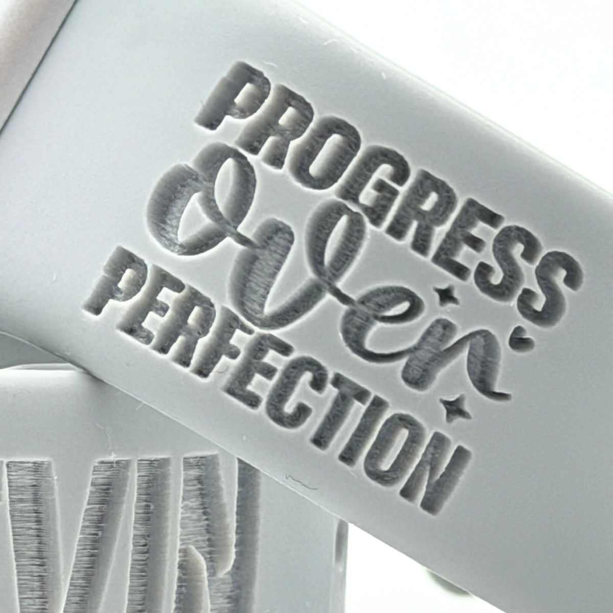 Engraving detail of the Progress Over Perfection Bold design on a grey silicone Progress Over Perfection watch band for Apple Watch