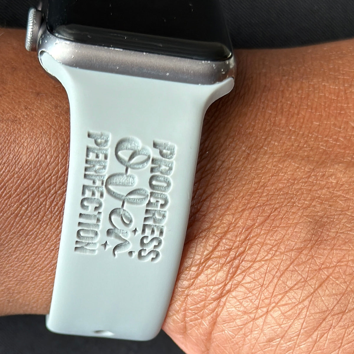 Grey Progress Over Perfection watch band for Apple Watch engraved with the Progress Over Perfection design, worn on a wrist with silver bracelets